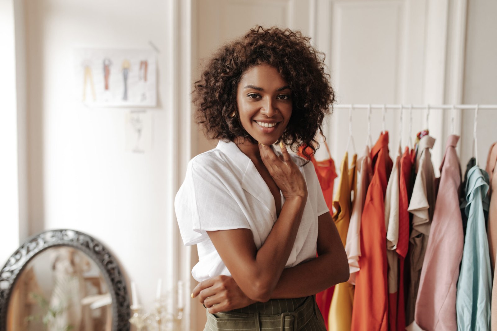 charming curly woman white blouse smiles sincerely looks front poses cozy dressing room