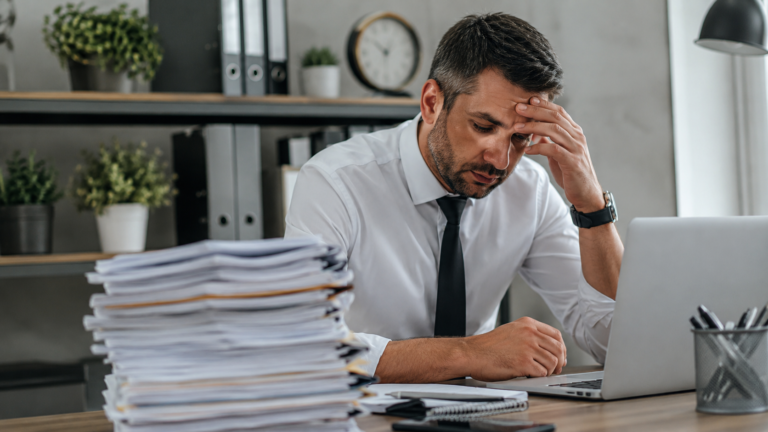Servidor público em ambiente administrativo analisando documentos e demonstrando preocupação com o acúmulo de trabalho e a ausência de férias, representando os desafios relacionados às férias não concedidas no serviço público.